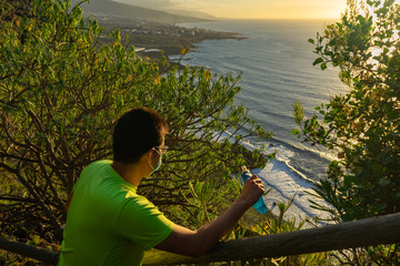 Runner looking at the coast of Tenerife. The man has a mask and a bottle of water (soft flask). He is resting and enjoying the views of a black sand beach.