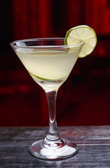 Vertical view. Cocktail with lime and rim, standing on the bar counter, isolated on a dark light background.