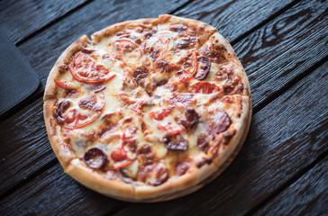 Big tasty pizza with sausage and tomatoes. Delicious pizza on a wooden background. Italian cuisine