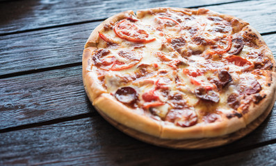 Round pizza on a wooden background. Delicious pizza with hunting sausage, olives and tomatoes. Italian cuisine