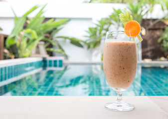 Mixed fruit and vegetables smoothie drink on swimming pool edge over blurred garden background, outdoor day light, healthy life style, diet drink