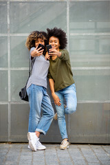 Full body two happy young black women taking selfie with cellphones