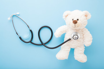 Stethoscope and white teddy bear on light blue table background. Pastel color. Doctor tool. People...