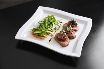 Beef steaks and toasts with avocado and rucola.