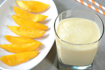 Mango milkshake in a glass cup and fresh cut mangoes in a plate