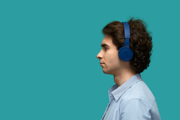 Sound contents. Profile portrait of a young beautiful man in blue headphones enjoying sounds