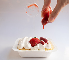sweet strawberry short cake on wooden background, with hand holding strawberry sauce