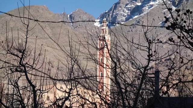 Moroccan mosque of Aroumd behind bushes silhouettes and with snowy mountains at the back, in the moroccan Atlas.
High angle slow motion, traveling movement, HD