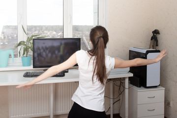 Fototapeta na wymiar Dancing at home during the quarantine of the coronavirus pandemic. Young woman doing exercises, looking at the monitor, is on self-isolation