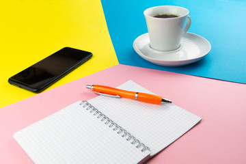 a Cup of coffee, smartphone and Notepad are placed on a multi-colored background