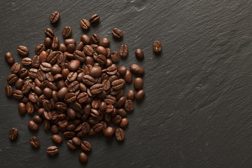 Pile of freshly roasted coffee beans on a grey slate.