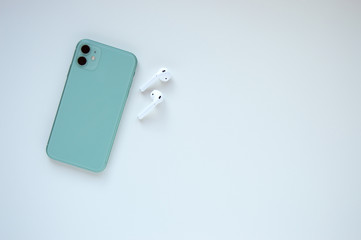 A modern mint-colored smartphone with two wireless headphones on a white background. Modern and...