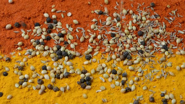 Falling spices black pepper, cumin, fenugreek, coriander seeds on red chilli and turmeric powder background