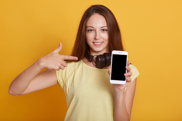 Closeup portrait of happy brunette female wearing casual t shirt, holding phone with blank screen...