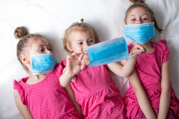 Three happy girls in pink dresses and protective medical masks. Protection against the coronavirus and influenza pandemic, home quarantine