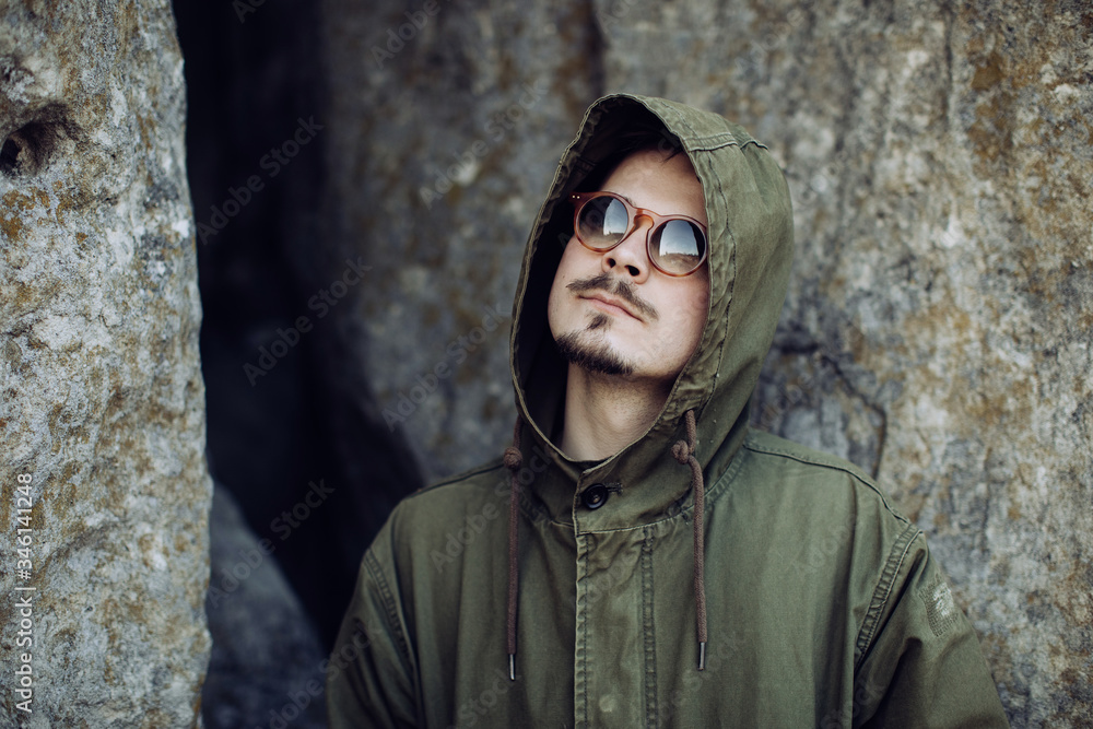 Wall mural Portrait of a young stylish man in a hood in the mountains