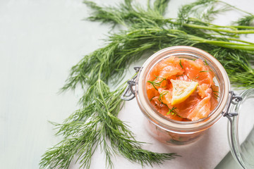 Slices of homemade smoked salmon with dill and lemon in jar on light background. Top view. Healthy food