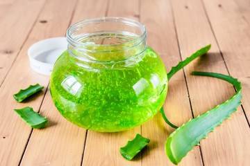 Extract of organic aloe vera gel and green aloe leaves on wooden background.