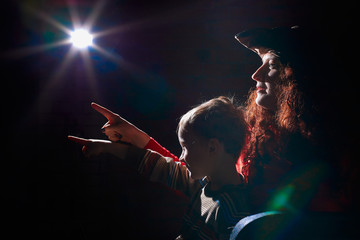 Ugle oman in red sweater and pirate hat with curly hair posing with small boy on black background....