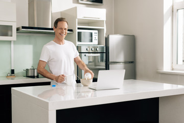 happy freelancer holding bottle and pouring milk in bowl near laptop