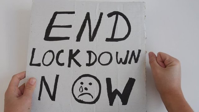 4k video of woman holding protest poster with words 'End Lockdown Now'. Woman moving banner up and down and hits table with fist. Anti lockdown. Coronavirus COVID-19 protest banner.