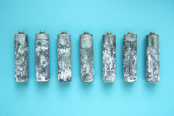 Seven heavily oxidized AA batteries unwrapped and laid out in a row on a blue background.