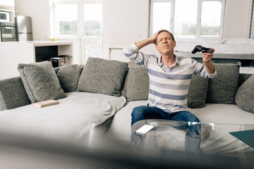 KYIV, UKRAINE - APRIL 14, 2020: selective focus of upset man touching head and holding joystick near smartphone with white screen on coffee table