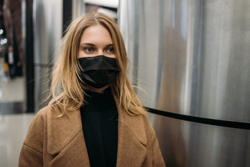 Young woman black medical mask, in coat standing in subway.