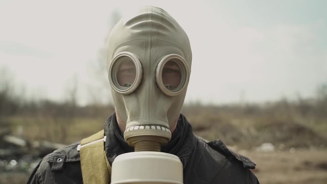 A guy in a gas mask nods to the camera. average plan. on the background dump