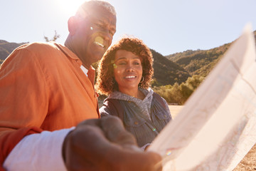 Senior Couple Looking At Map As They Hike Along Trail In Countryside Together