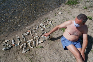 Man on the beach, summer vacation in the time of coronavirus pandemic, older man with protective surgery mask sunbathing on the river bank, covid 19