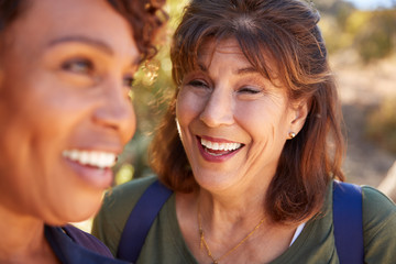 Two Senior Female Friends Hiking Along Trail In Countryside Together