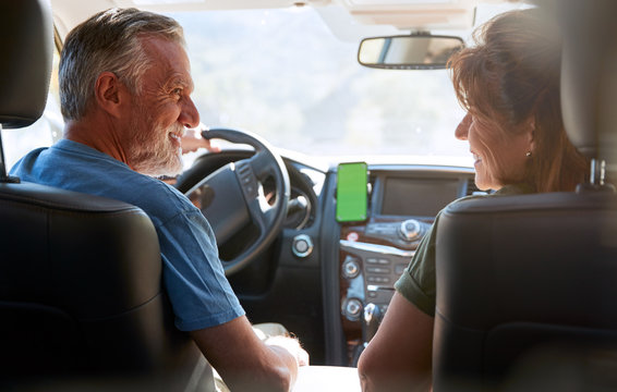 Senior Hispanic Couple On Drive Through Countryside Using Sat Nav On Mobile Phone