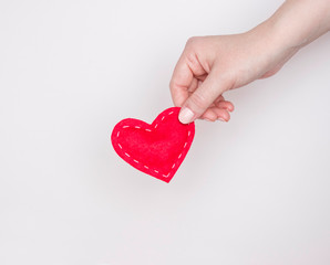 Concept of love, heart treatment. A woman's hand holds a red rag heart. Light background.