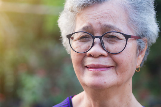 A portrait of an elderly woman wearing eyeglasses, smiling and looking at the camera while standing in a garden. Space for text. Concept of old people and healthcare