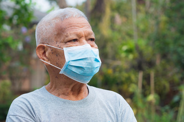 A portrait of an elderly man wearing a face mask looking away while standing in a garden. Mask for protect virus, coronavirus, pollen grains. Concept of old people and healthcare