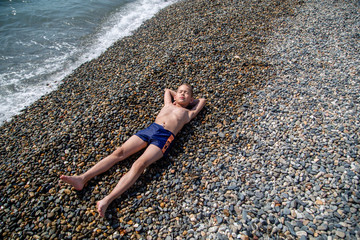 boy resting on a pebble beach by the sea © vitec40