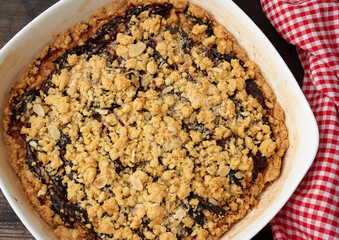 baked crumble pie with blue plum in a white ceramic plate on a wooden table