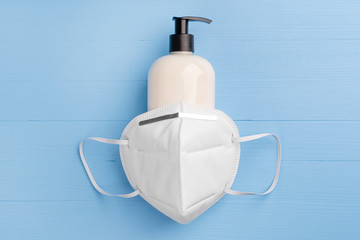 n95 respiratory mask covers a plastic container with mild soap and a black dispenser. On a light blue wooden background. Coronavirus and influenza prevention concept