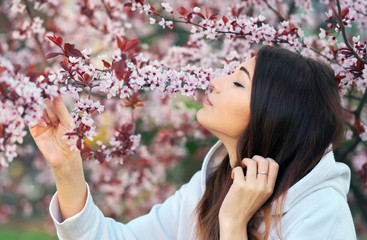 Smiling beautiful girl standing near a peach tree during sunset. Happy face. Spring time.