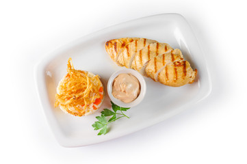Baked chicken breast with sauce and rice with vegetables on a white rectangular plate on white background, top view