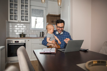 Young father working remotely while babysitting his son.