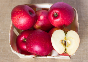 Red apples in a wooden basket box, out of focus and two halves cut with seeds on a homespun linen napkin, summer healthy fruits vitamins, juicy dessert and snack