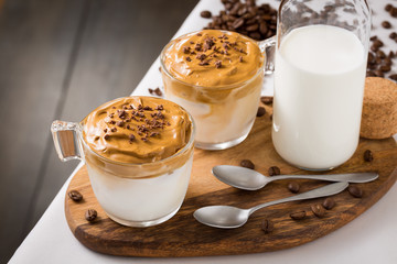 Whipped dalgona coffee and milk jug on table with coffee beans scattered around - ダルゴナコーヒー