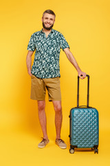 full length view of happy bearded guy with travel bag on yellow