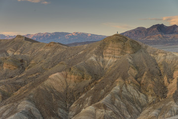 A lone man stands on top of a peak next to Manly Beacon in Death Valley, California, USA.