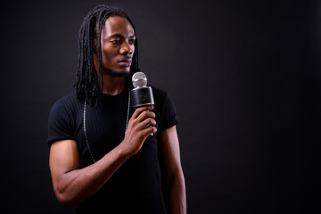 Portrait of young handsome African man with dreadlocks using microphone