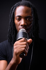 Face of young handsome African man with dreadlocks using microphone