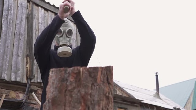 The guy in the gas mask with an ax colitis firewood. slow motion. blurred background. average plan