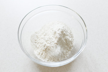 Glass bowl with flour on a light background. Flour ingredient, top view.